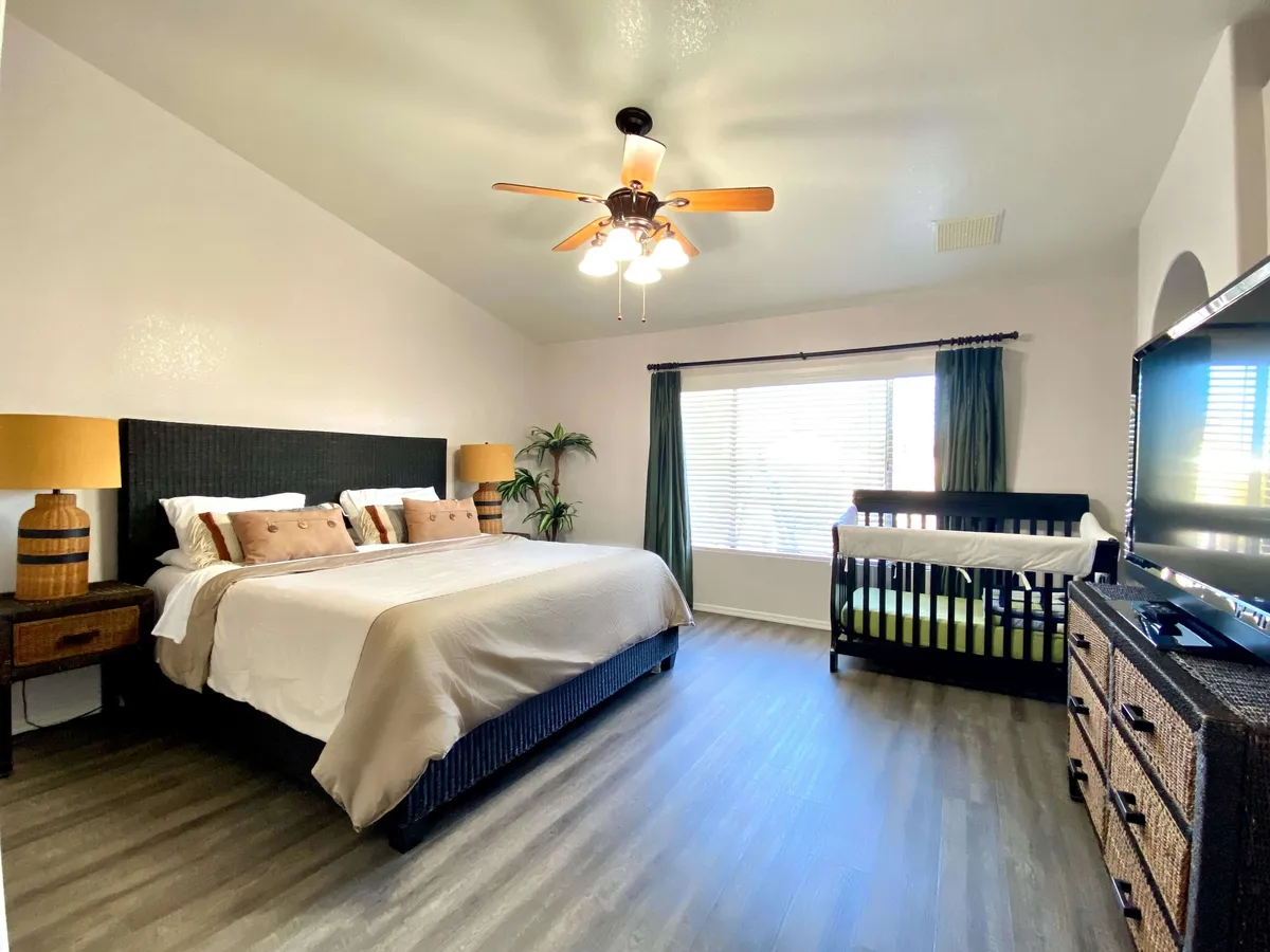 A spacious master bedroom featuring a king-sized bed with soft linens, a crib positioned conveniently for parents traveling with young children, and a TV mounted opposite the bed. The space feels serene and welcoming, perfect for restful family nights.