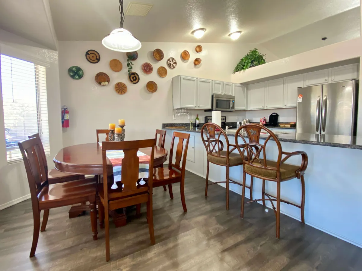 A spacious dining area with a large table set for guests, adjacent to a kitchen bar and decorated with charming wall plates. The arrangement is ideal for family meals, celebrations, and casual gatherings, with seating that invites conversation and connection.