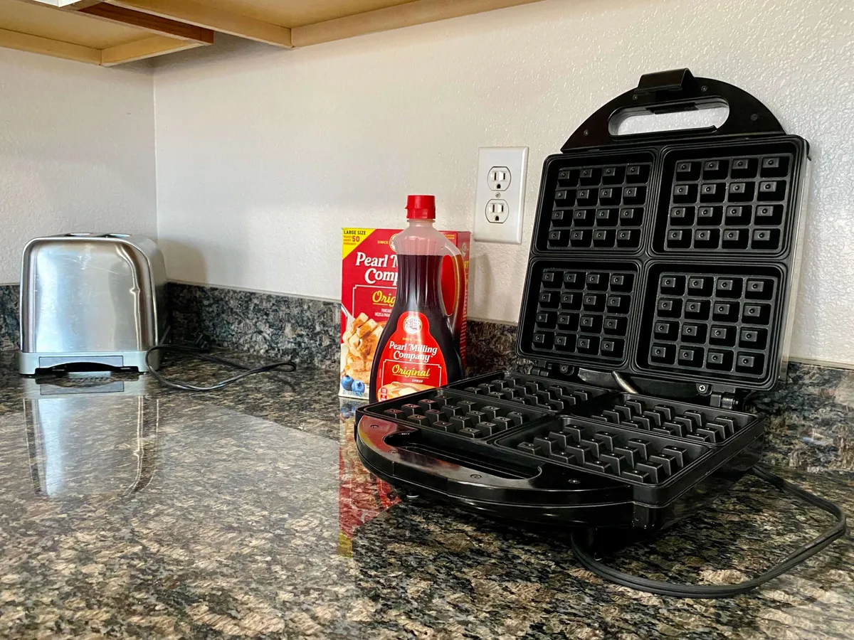A close-up of a cheerful breakfast station, featuring a waffle maker, toaster, syrup bottle, and waffle mix box. The setup is ready for cooking breakfast together, evoking the joy of morning routines and shared traditions.