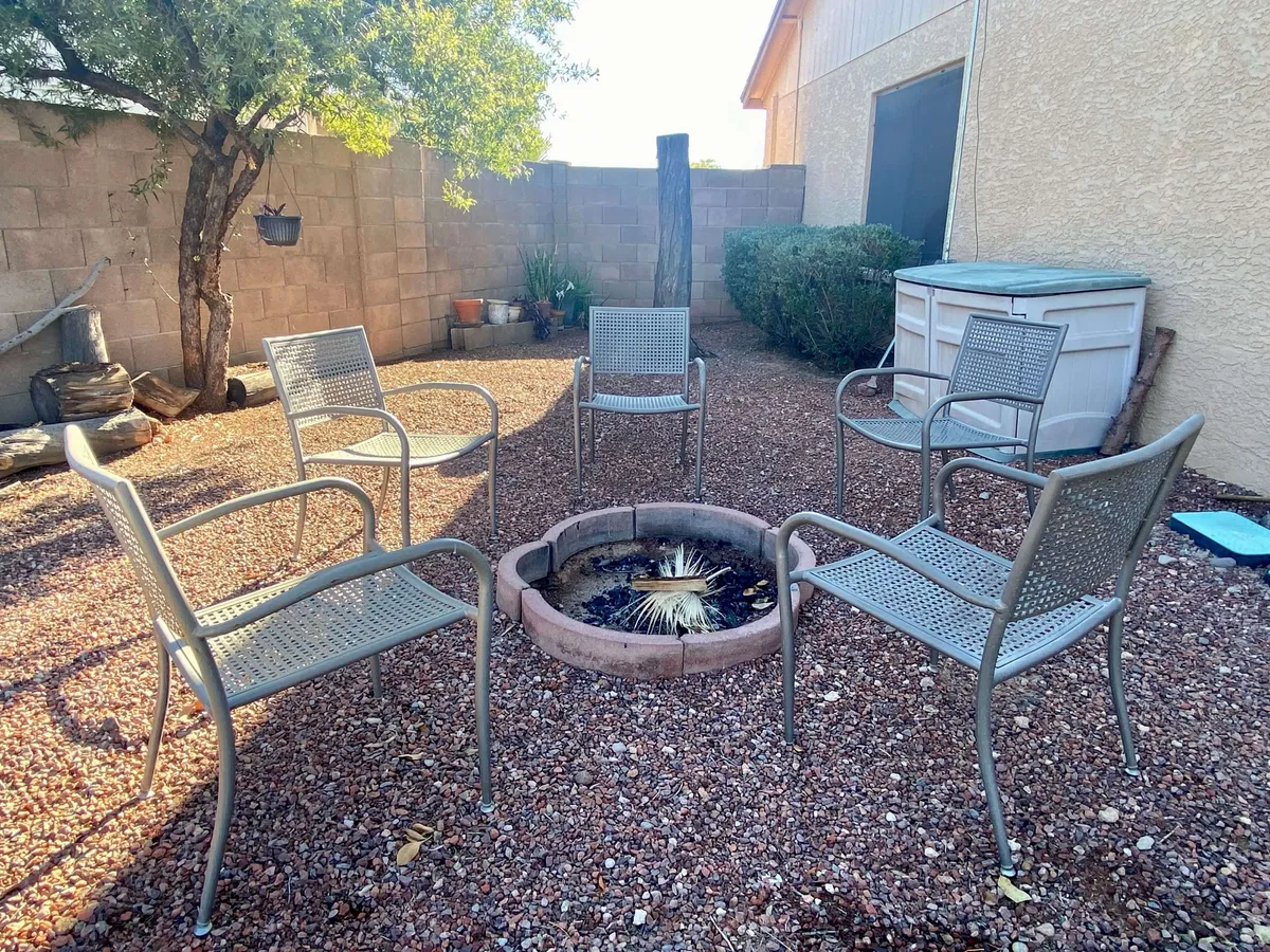 A cozy fire pit area with ample outdoor seating and surrounding plants, ideal for gatherings and evening relaxation. The inviting setup encourages storytelling and social moments around the warmth of the fire.