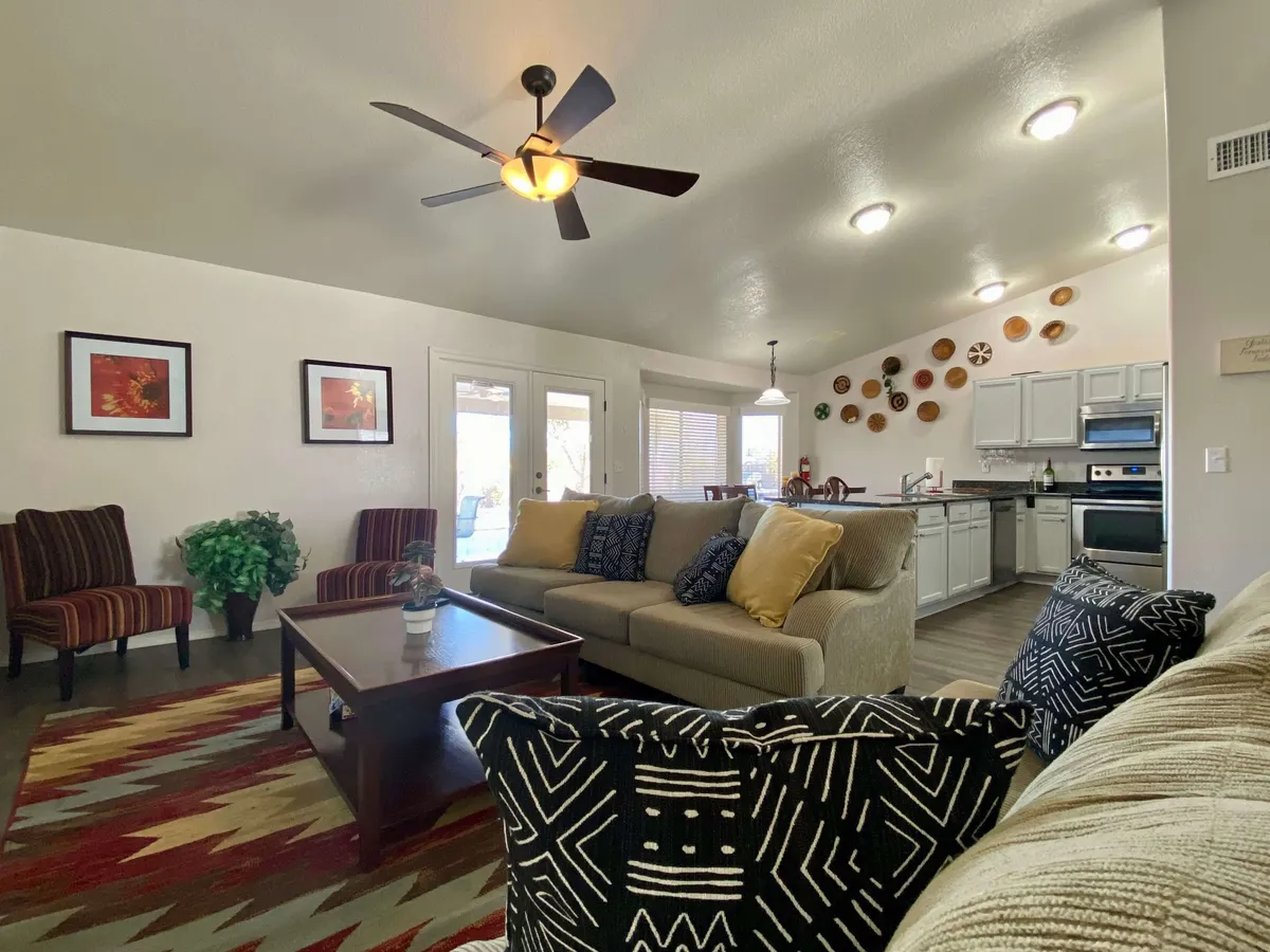 An open-concept interior where a cozy sofa with colorful pillows takes center stage, while the dining area is clearly visible in the background. Artful touches and a ceiling fan add to the inviting vibe, showcasing the seamless flow between spaces.