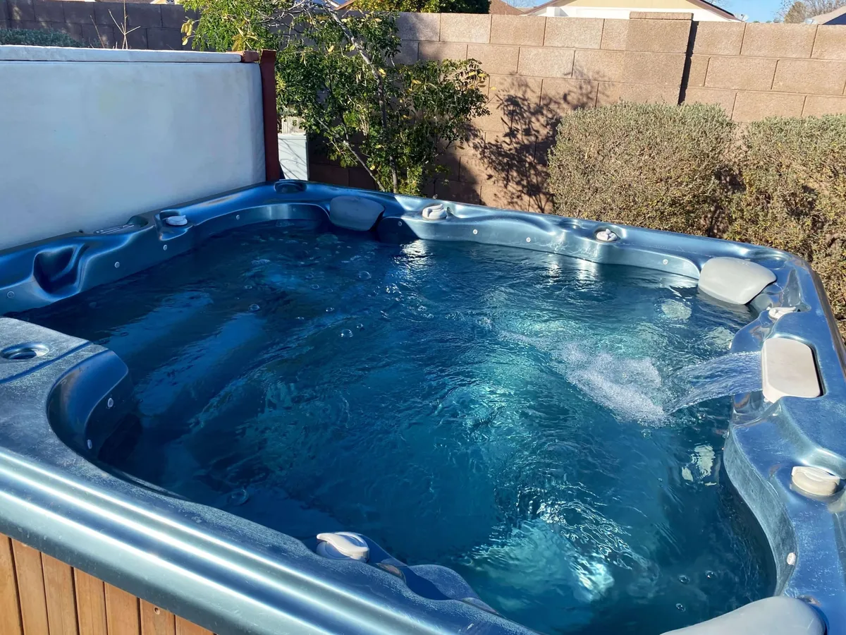 A cozy outdoor area featuring a bubbling hot tub surrounded by greenery and a brick wall for privacy. The mood is relaxed and inviting, ideal for unwinding after a day of local exploration and adventure.