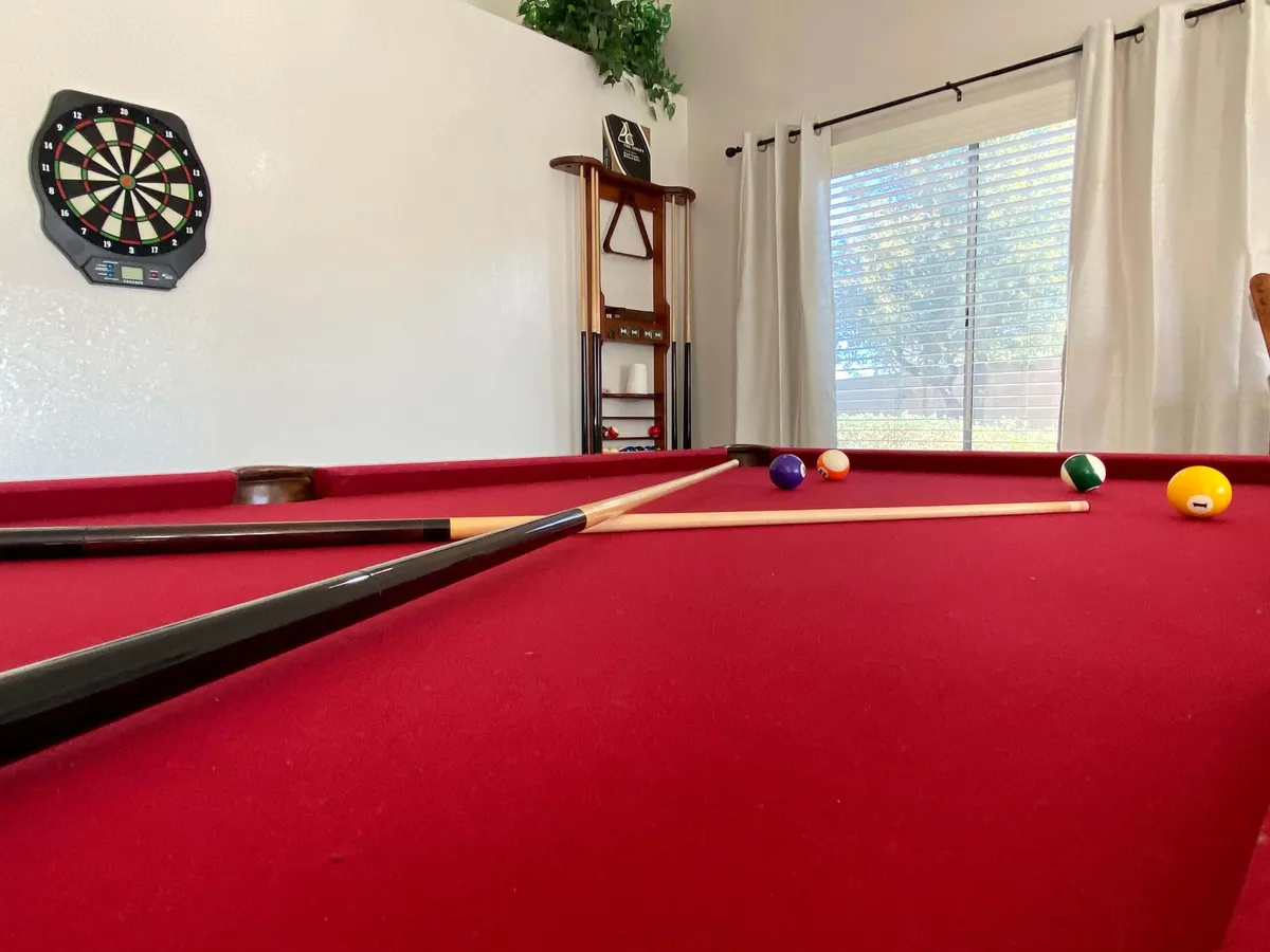 A lively interior scene with a pool table, dartboard, and a window with curtains, evoking recreational energy. The space is designed for games, socializing, and friendly competitions among friends or family.