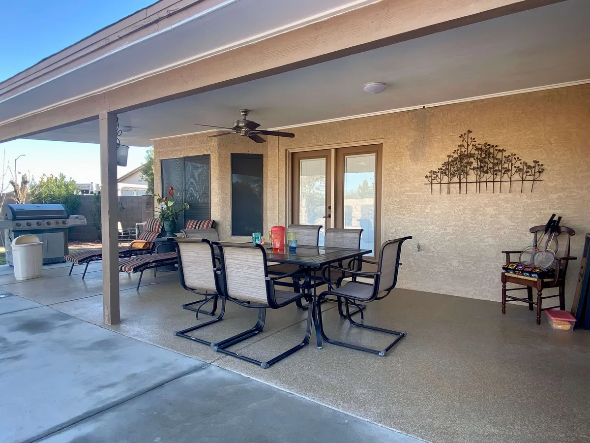 A stylish patio area showcasing a large outdoor dining table, a grill station, comfortable seating, and decorative wall art. The covered space is ideal for festive meals, barbecues, and casual lounging.